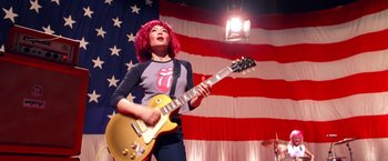 Movie still from “Charlie's Angels” (2000), directed by McG – A woman with pink hair holding a gold guitar; Medium shot, Low angle