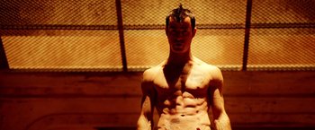 Movie still from “Charlie's Angels: Full Throttle” (2003), directed by McG – A man with no shirt is standing in front of a chain link fence; Medium shot, Low angle