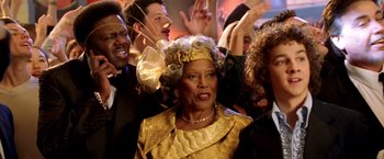 Movie still from “Charlie's Angels: Full Throttle” (2003), directed by McG – An older woman wearing a gold dress and a gold hat; Close Up shot, Over the shoulder angle