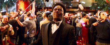 Movie still from “Charlie's Angels: Full Throttle” (2003), directed by McG – A man in a suit and bow tie holding a camera in front of a crowd of onlookers; Close Up shot, Low angle