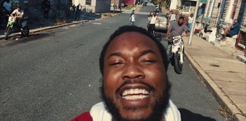 Movie still from “Charm City Kings” (2020), directed by Angel Manuel Soto – A person smiling on a street; Close Up shot, High angle