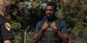 Movie still from “Charm City Kings” (2020), directed by Angel Manuel Soto – A man in a police uniform adjusting his vest; Medium shot, Over the shoulder angle