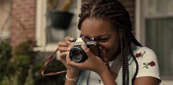 Movie still from “Charm City Kings” (2020), directed by Angel Manuel Soto – A young woman holding a camera taking a picture; Close Up shot, Over the shoulder angle
