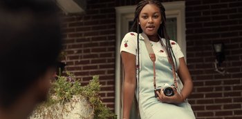 Movie still from “Charm City Kings” (2020), directed by Angel Manuel Soto – A woman holding a camera in front of a brick building; Medium shot, Low angle