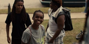 Movie still from “Charm City Kings” (2020), directed by Angel Manuel Soto – A young boy smiling for the camera while standing next to other people; Medium shot, Over the shoulder angle