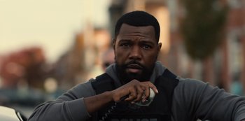 Movie still from “Charm City Kings” (2020), directed by Angel Manuel Soto – A man in a police vest holding a phone; Close Up shot, Over the shoulder angle