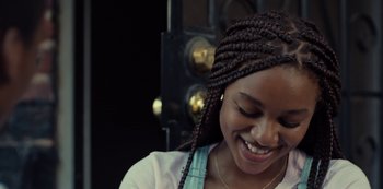 Movie still from “Charm City Kings” (2020), directed by Angel Manuel Soto – A young woman smiles brightly while wearing braids; Close Up shot, Over the shoulder angle