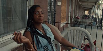 Movie still from “Charm City Kings” (2020), directed by Angel Manuel Soto – A woman sitting on top of a chair on a porch; Close Up shot, Over the shoulder angle