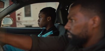 Movie still from “Charm City Kings” (2020), directed by Angel Manuel Soto – A young boy sitting in a car with a man in the back seat; Close Up shot, Over the shoulder angle