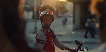 Movie still from “Charm City Kings” (2020), directed by Angel Manuel Soto – A young boy wearing a helmet riding a bike; Close Up shot, Over the shoulder angle
