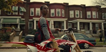 Movie still from “Charm City Kings” (2020), directed by Angel Manuel Soto – A man riding on the back of a red motorcycle; Medium shot, Low angle