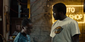 Movie still from “Charm City Kings” (2020), directed by Angel Manuel Soto – A man and a woman standing next to each other in a room; Medium shot, Over the shoulder angle