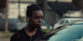 Movie still from “Charm City Kings” (2020), directed by Angel Manuel Soto – A young man with headphones looking at his reflection in a car mirror; Close Up shot, Over the shoulder angle