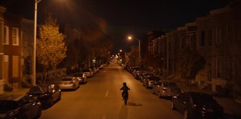 Movie still from “Charm City Kings” (2020), directed by Angel Manuel Soto – A person riding a motorcycle down the middle of a street at night; Extreme Wide shot, High angle