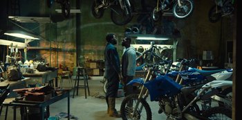 Movie still from “Charm City Kings” (2020), directed by Angel Manuel Soto – Two men standing in front of motorcycles in a garage; Wide shot, Over the shoulder angle