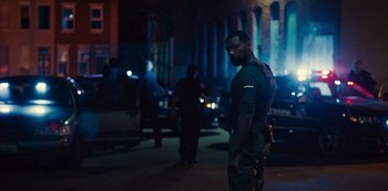 Movie still from “Charm City Kings” (2020), directed by Angel Manuel Soto – A man standing on the side of the street at night; Medium shot, Over the shoulder angle