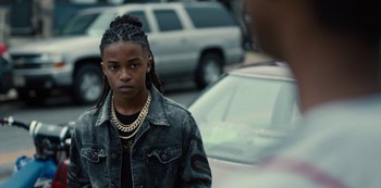 Movie still from “Charm City Kings” (2020), directed by Angel Manuel Soto – A young man in a denim jacket and gold chains; Close Up shot, Over the shoulder angle