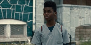 Movie still from “Charm City Kings” (2020), directed by Angel Manuel Soto – A young man wearing a gray shirt and a red and white striped shirt; Close Up shot, Over the shoulder angle