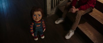 Movie still from “Child's Play” (2019), directed by Lars Klevberg – A child's play chucky doll sitting on the floor next to a person; Medium shot, Over the shoulder angle