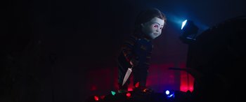 Movie still from “Child's Play” (2019), directed by Lars Klevberg – A creepy doll with a knife on top of a pile of christmas lights; Medium shot, Low angle