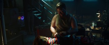 Movie still from “Child's Play” (2019), directed by Lars Klevberg – A man is shaving a doll's head in a dark room; Medium shot, Over the shoulder angle