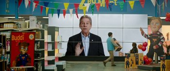 Movie still from “Child's Play” (2019), directed by Lars Klevberg – A man in a black suit is in front of a large screen; Wide shot, Over the shoulder angle
