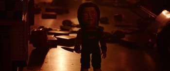 Movie still from “Child's Play” (2019), directed by Lars Klevberg – A creepy doll with a knife in its mouth; Medium shot, High angle