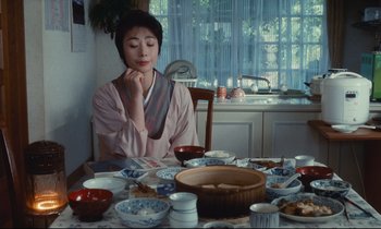 Movie still from “Chizuko's Younger Sister” (1991), directed by Nobuhiko Ôbayashi – A person sitting at a table with a lot of dishes on it; Medium shot, Low angle
