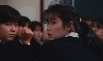Movie still from “Chizuko's Younger Sister” (1991), directed by Nobuhiko Ôbayashi – A young girl is sitting in front of a group of people; Close Up shot, Over the shoulder angle