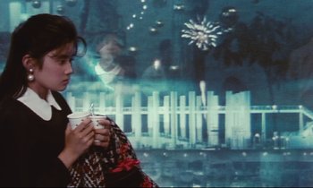 Movie still from “Chizuko's Younger Sister” (1991), directed by Nobuhiko Ôbayashi – A woman is holding a cup of coffee in front of a fence; Medium shot, Over the shoulder angle