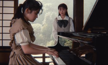 Movie still from “Chizuko's Younger Sister” (1991), directed by Nobuhiko Ôbayashi – Two young girls are playing a piano in front of a window; Medium shot, Low angle