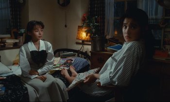 Movie still from “Chizuko's Younger Sister” (1991), directed by Nobuhiko Ôbayashi – Two women sitting on a chair in front of a lamp; Medium shot, High angle