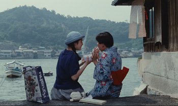 Movie still from “Chizuko's Younger Sister” (1991), directed by Nobuhiko Ôbayashi – Two women sitting on a dock near a body of water; Medium shot, Low angle