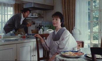 Movie still from “Chizuko's Younger Sister” (1991), directed by Nobuhiko Ôbayashi – A woman sitting at a table in front of a plate of food; Medium shot, Over the shoulder angle