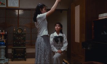 Movie still from “Chizuko's Younger Sister” (1991), directed by Nobuhiko Ôbayashi – A woman standing in front of a woman sitting in a chair; Medium shot, Low angle