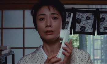 Movie still from “Chizuko's Younger Sister” (1991), directed by Nobuhiko Ôbayashi – A woman holding a remote control in her hand; Close Up shot, Low angle