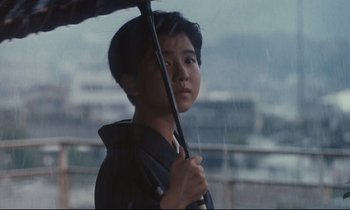 Movie still from “Chizuko's Younger Sister” (1991), directed by Nobuhiko Ôbayashi – A young man holding an open umbrella in the rain; Close Up shot, Low angle