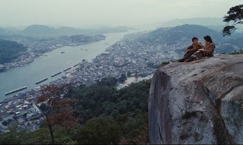 Movie still from “Chizuko's Younger Sister” (1991), directed by Nobuhiko Ôbayashi – A man sitting on top of a cliff overlooking a city; Extreme Wide shot, High angle