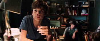 Movie still from “The Dark Tower” (2017), directed by Nikolaj Arcel – A young man sitting at a table in front of a bookshelf; Close Up shot, Low angle