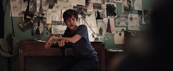 Movie still from “The Dark Tower” (2017), directed by Nikolaj Arcel – A young man sitting in front of a wall of pictures; Medium shot, High angle