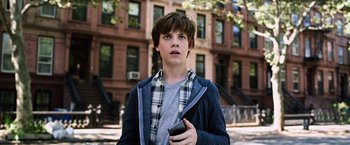 Movie still from “The Dark Tower” (2017), directed by Nikolaj Arcel – A young man holding a cell phone while standing in front of a building; Close Up shot, Low angle