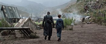 Movie still from “The Dark Tower” (2017), directed by Nikolaj Arcel – A man and a boy walking down a dirt road; Wide shot, Over the shoulder angle