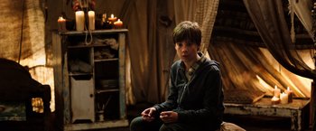 Movie still from “The Dark Tower” (2017), directed by Nikolaj Arcel – A young boy sitting in a room with candles; Medium shot, Over the shoulder angle