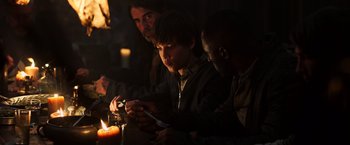 Movie still from “The Dark Tower” (2017), directed by Nikolaj Arcel – A group of people sitting around a candle lit table; Medium shot, High angle