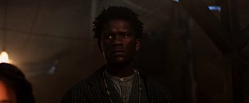 Movie still from “The Dark Tower” (2017), directed by Nikolaj Arcel – A man in a jacket and a necklace is looking at the camera; Close Up shot, Low angle