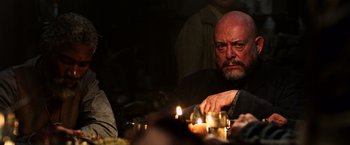Movie still from “The Dark Tower” (2017), directed by Nikolaj Arcel – A man sitting in front of a group of candles on top of a table; Close Up shot, Over the shoulder angle