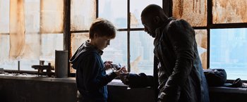 Movie still from “The Dark Tower” (2017), directed by Nikolaj Arcel – Two people looking at a cell phone in front of a window; Medium shot, Over the shoulder angle