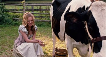 Movie still from “Choke” (2008), directed by Clark Gregg – A woman sitting in front of a black and white cow in a field; Medium shot, High angle