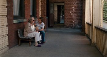 Movie still from “Choke” (2008), directed by Clark Gregg – A man and a woman sitting on a wooden bench; Wide shot, Over the shoulder angle