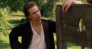 Movie still from “Choke” (2008), directed by Clark Gregg – A man leaning against a wooden post in a field; Medium shot, Over the shoulder angle